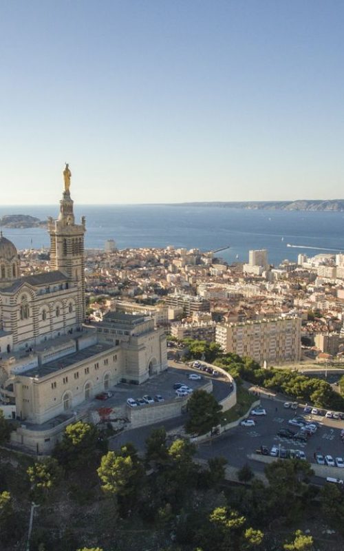 High angle view of cityscape by sea. Notre Dame de la Garde in Marseille against clear sky. Buildings by seascape on sunny day.